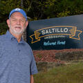 A man stands in front of a sign that reads, “Saltillo Mississippi, Welcome Home.”