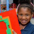 A young girl smiles and holds up a Lego creation.