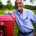 Smiling man in gingham dress shirt leans on a tractor