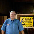 Paul Cavanaugh standing in front of a sign that reads Master Gardeners at Work.