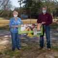 A man and woman wearing masks hold each side of a banner that reads “2020 Winner $2,500.”