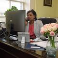 A woman sits behind a desktop computer at a desk talking on the phone.