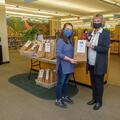 Two masked women with glasses and brown hair holding a brown bag.