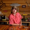 A man with glasses standing behind a table with shells, teeth, and bones on it.