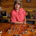 A man with glasses standing behind a table with shells, teeth, and bones on it.