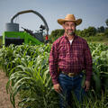 A man wearing a large hat and red shirt standing in a field.