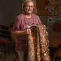 An older woman smiles while holding a quilt.