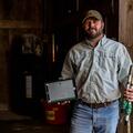 A man stands in a wooden shed holding parts to a soil sensor system.