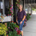 A woman standing outside beside flowers wreathing a door.