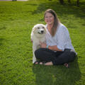 A woman, smiling, sitting with her arms around a large dog.