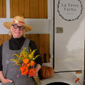 A woman with a straw hat and round-framed glasses holding a bunch of flowers and smiling.