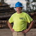 A man, smiling, wearing a hard hat and neon shirt with L&S Logging printed on it.