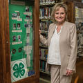A woman stands in front of library book shelves beside a tall, green 4-H display.