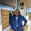 A woman standing beside the window of a house that has a sign with “Venisha’s Home” listed on it.