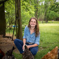 A girl wearing denim smiles as she feeds her chickens.
