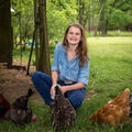 A girl wearing denim smiles as she feeds her chickens.