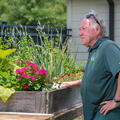 A man, standing beside a wooden table filled with plants, looking into the distance.
