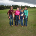 Five people smiling with three horses, all standing on a grassy plain