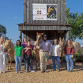 A group of men and women standing in front of a barn and alongside three horses.