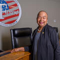 A woman stands smiling in front of the seal for Forest, MS, that lists “Leading the Way” across the bottom.