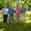 Four people standing outside, hands in their pockets.