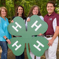 Three women and one man hold a large 4-H clover
