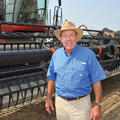 A man wearing a blue shirt and cowboy hat stands in front of a piece of farming machinery.