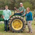 An older man, a woman, and a teenage boy around a green tractor.