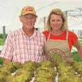 A man and woman behind plants in a greenhouse.