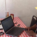 A woman sits on one side of a table, and a man with a laptop sits opposite from her.