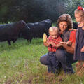 A woman and two small children in a field with black cows grazing behind them.