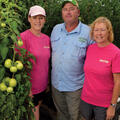 A young woman with an older man and woman standing next to a tomato plant.