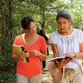 Two women walk and look at a book.