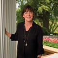 A woman wearing a black shirts rests one hand on a column of a house.