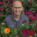 A smiling man with a polo listing his name as “Dr. Eddie Smith” is surrounded by colorful flowers.