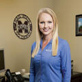 A smiling woman in a blue shirt poses for the camera.