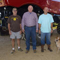 Three men and a dog stand in front of farm equipment.