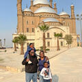 A Black man and woman standing with a boy and a girl in front of a mosque in the desert.