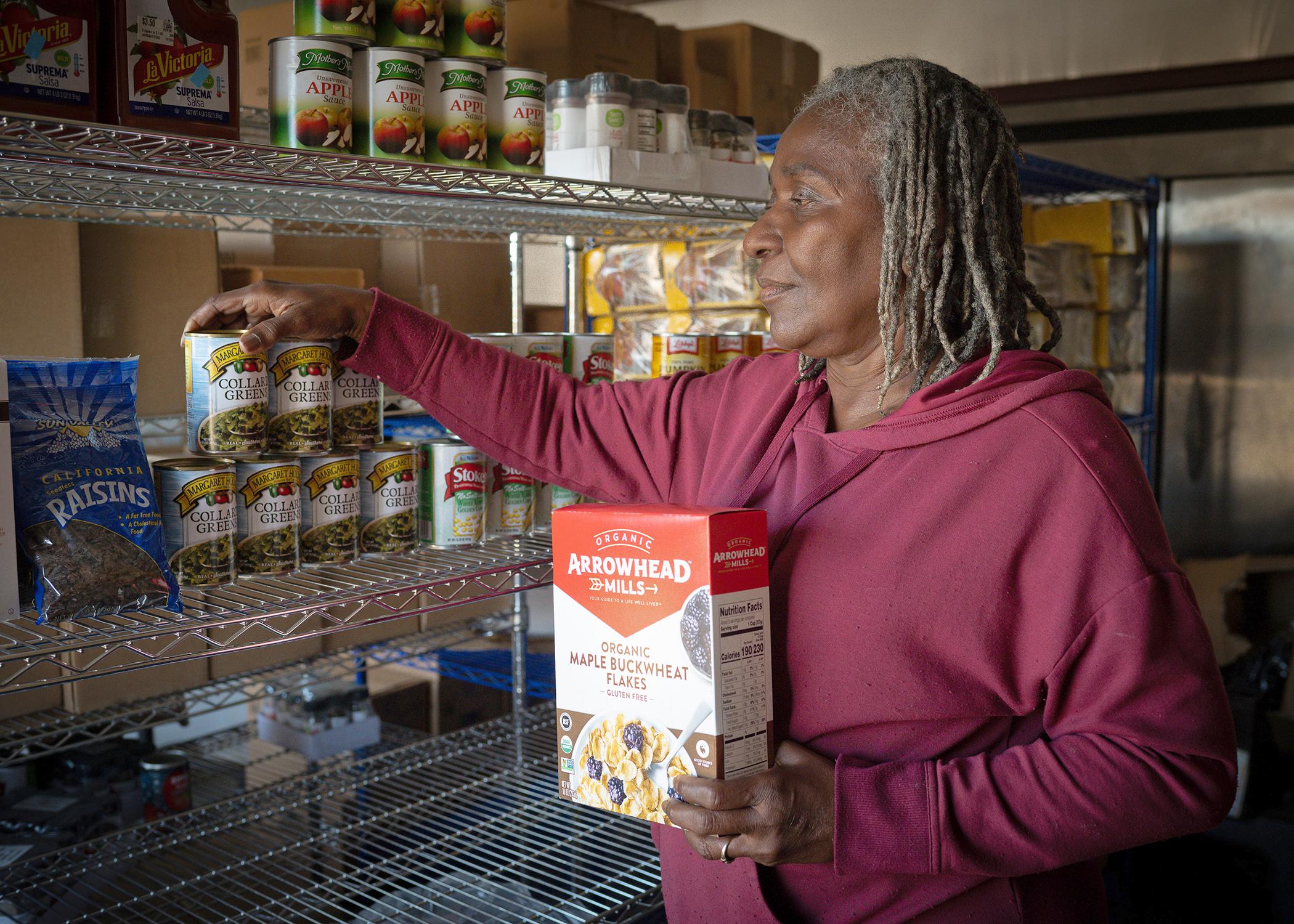 A woman puts nonperishable food on pantry shelves.
