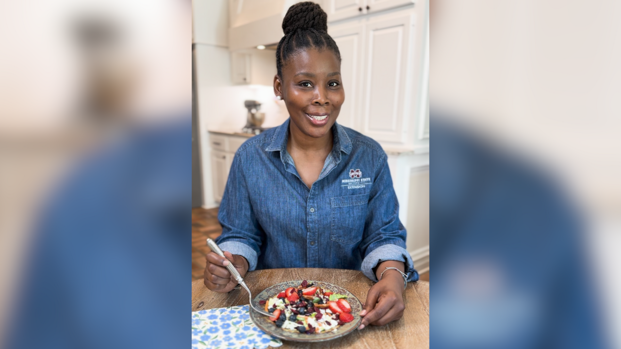 A woman sits at a kitchen table with a bowl of yogurt and berries.