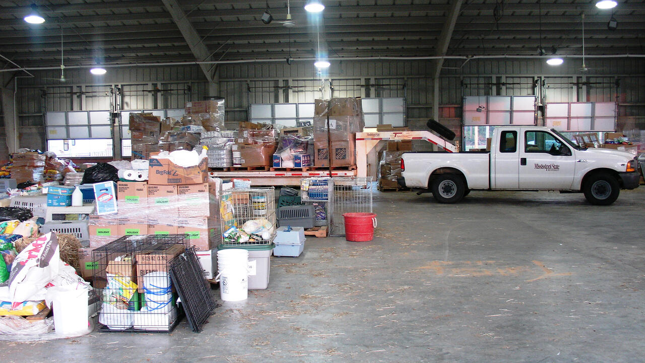 A white pickup truck inside a warehouse with boxes of household items behind it.