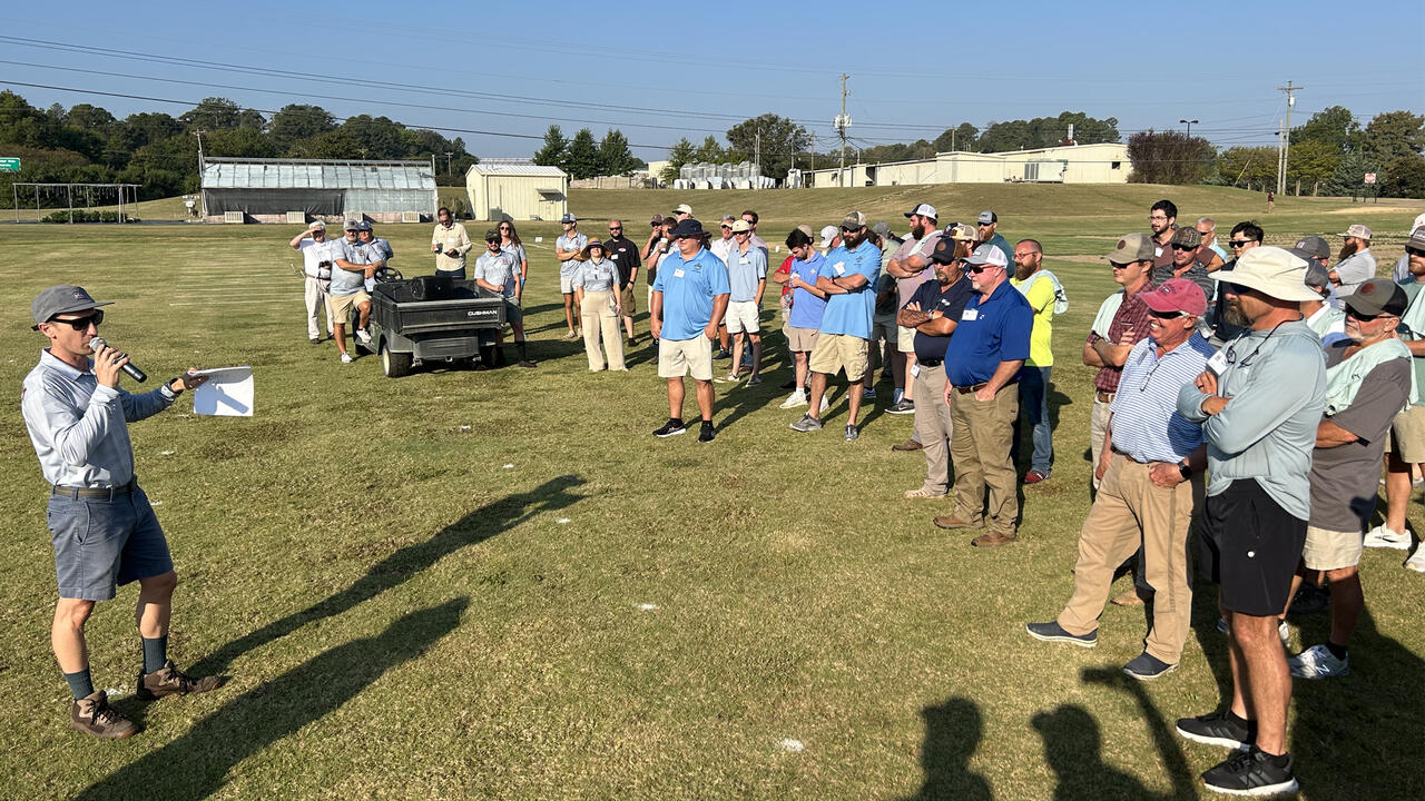 A presenter shows turf samples to a crowd of onlookers.
