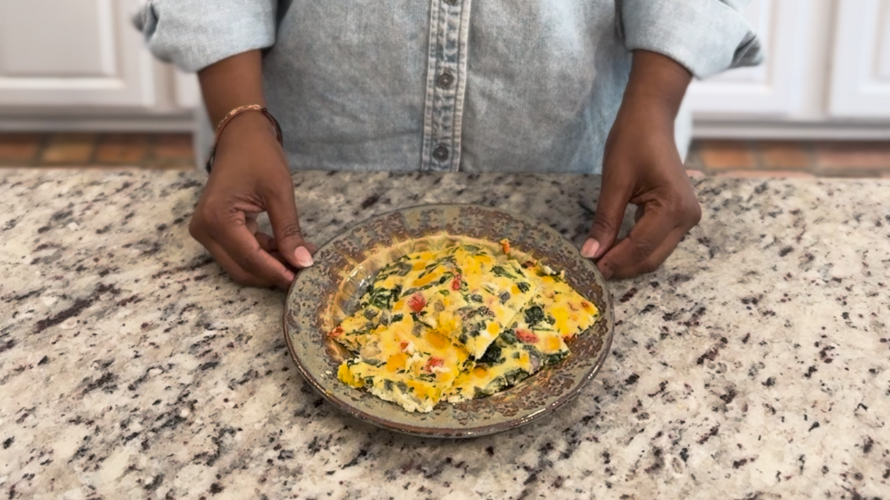 A woman stands at a kitchen counter with a plate of Sheet Pan Eggs and Veggies.
