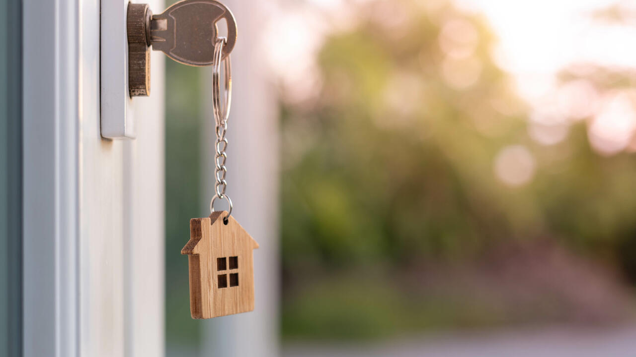 A house key on a house-shaped keychain is insterted in the front door lock of a home.