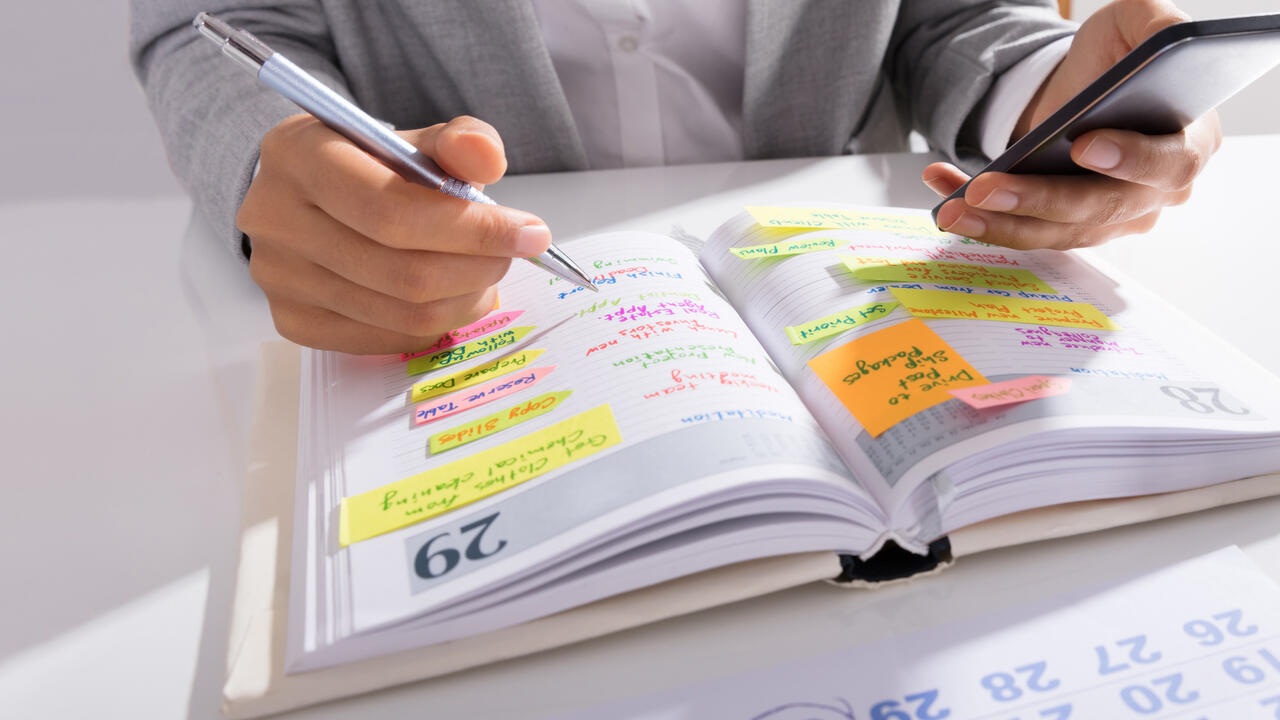 Person’s hands hold a mobile phone with a list of work on the desk.