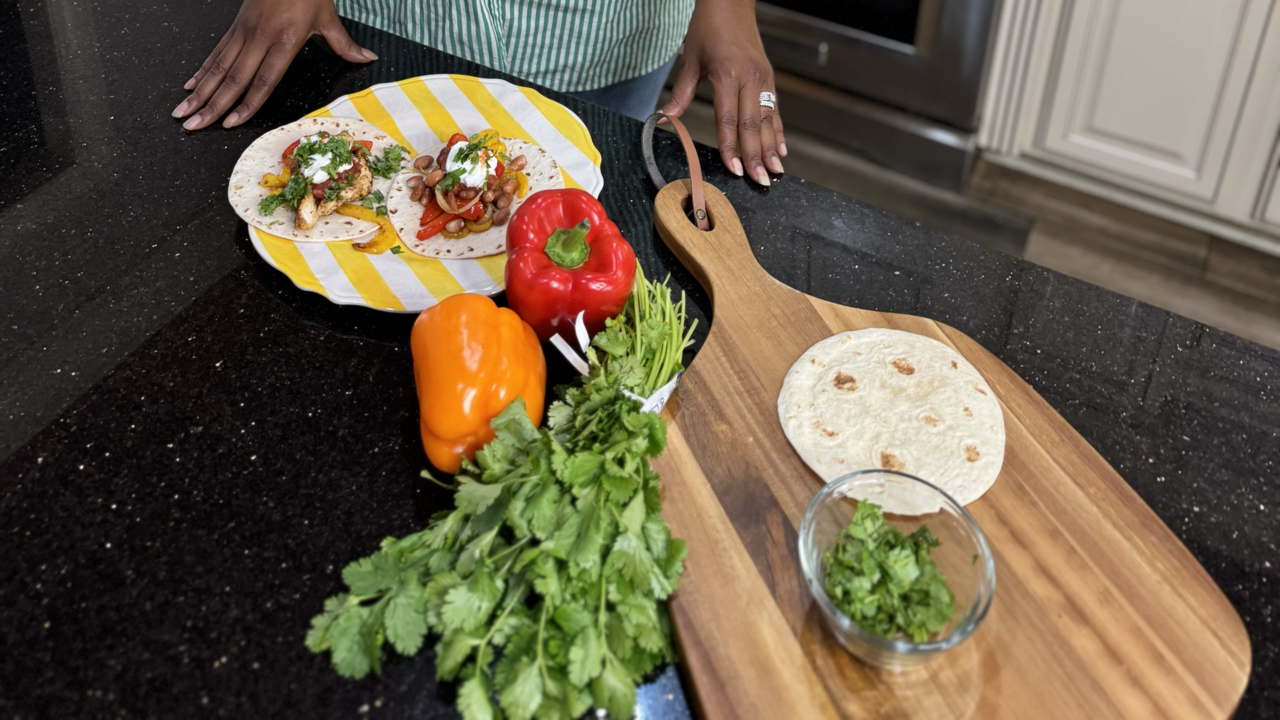 A woman in a kitchen with ingredients for fajitas on the counter.