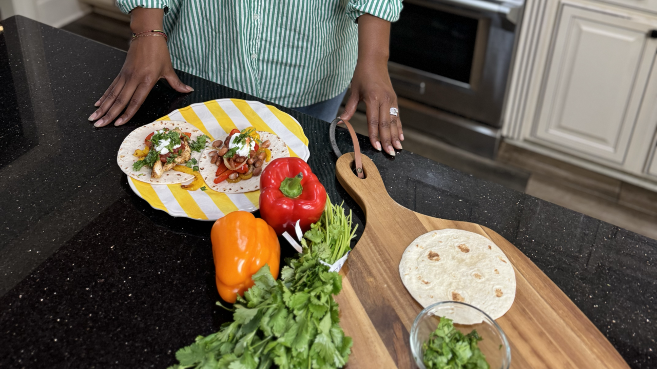 A woman in a kitchen with ingredients for fajitas on the counter.