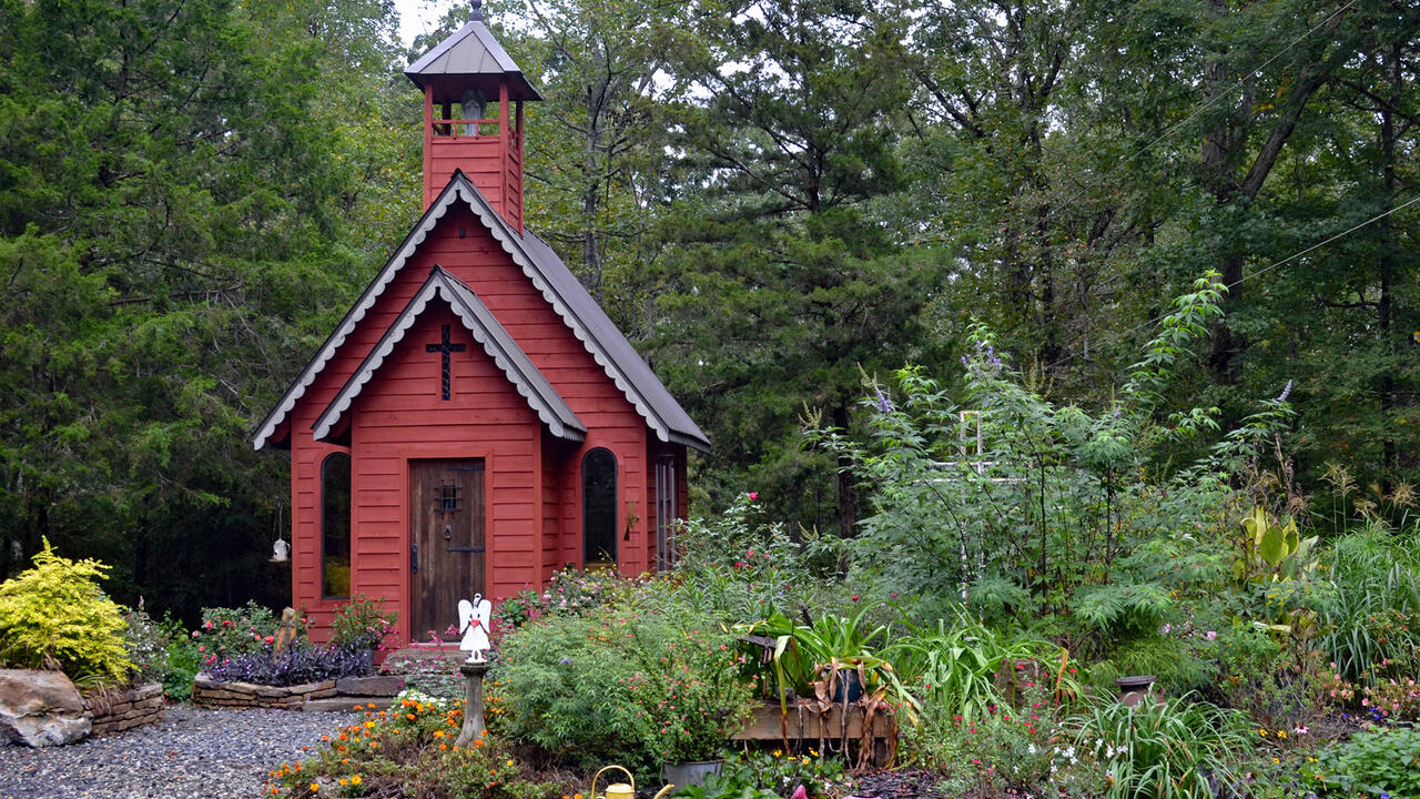 A small red structure stands in the center of a garden landscape.