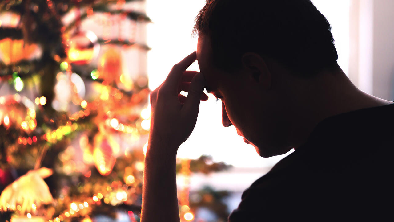 Man stressed out looking at a Christmas tree.