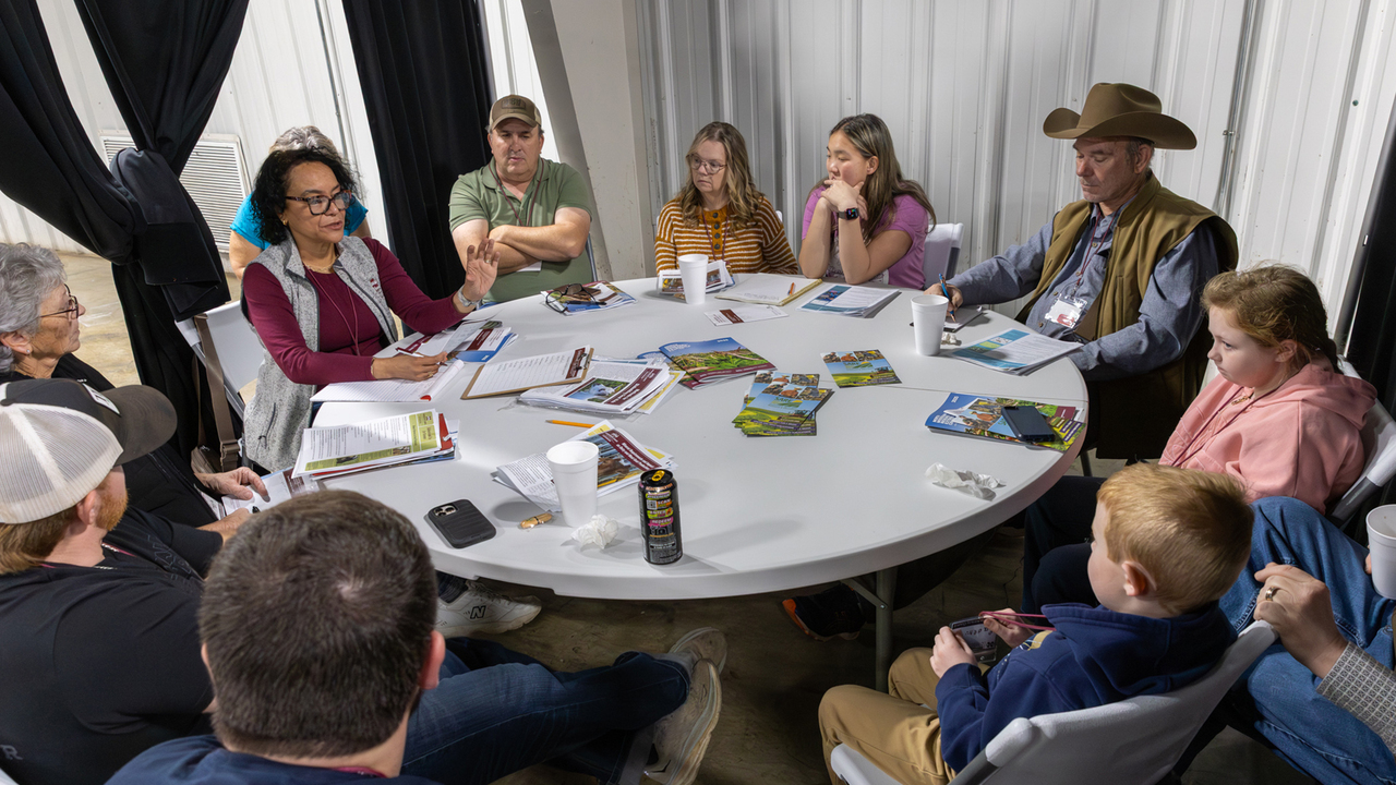 A circle of people sit in a meeting around a table.